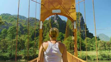 rear view of a young woman crossing a suspension footbridge over the nam song river in vang vieng, laos