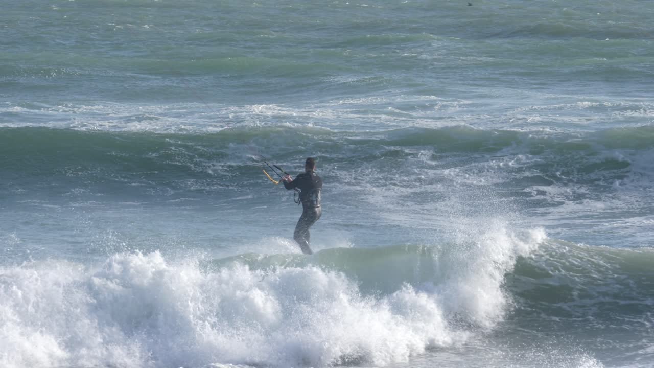 Kite surfer rides out over waves in Cape Town's Big Bay with strong wind and powerful surf