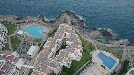 aerial shot of hotel complex with swimming pools on cliffs beside ocean in mallorca