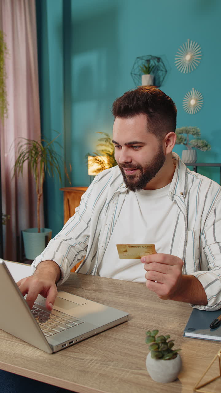 Un uomo d'affari felice che usa una carta di credito bancaria e un portatile per i pagamenti degli acquisti online in ufficio a casa