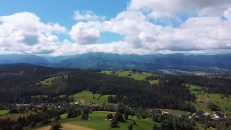 aerial shot in alpine village epic mountain peaks, hills covered with pine trees in haze, sunrise light