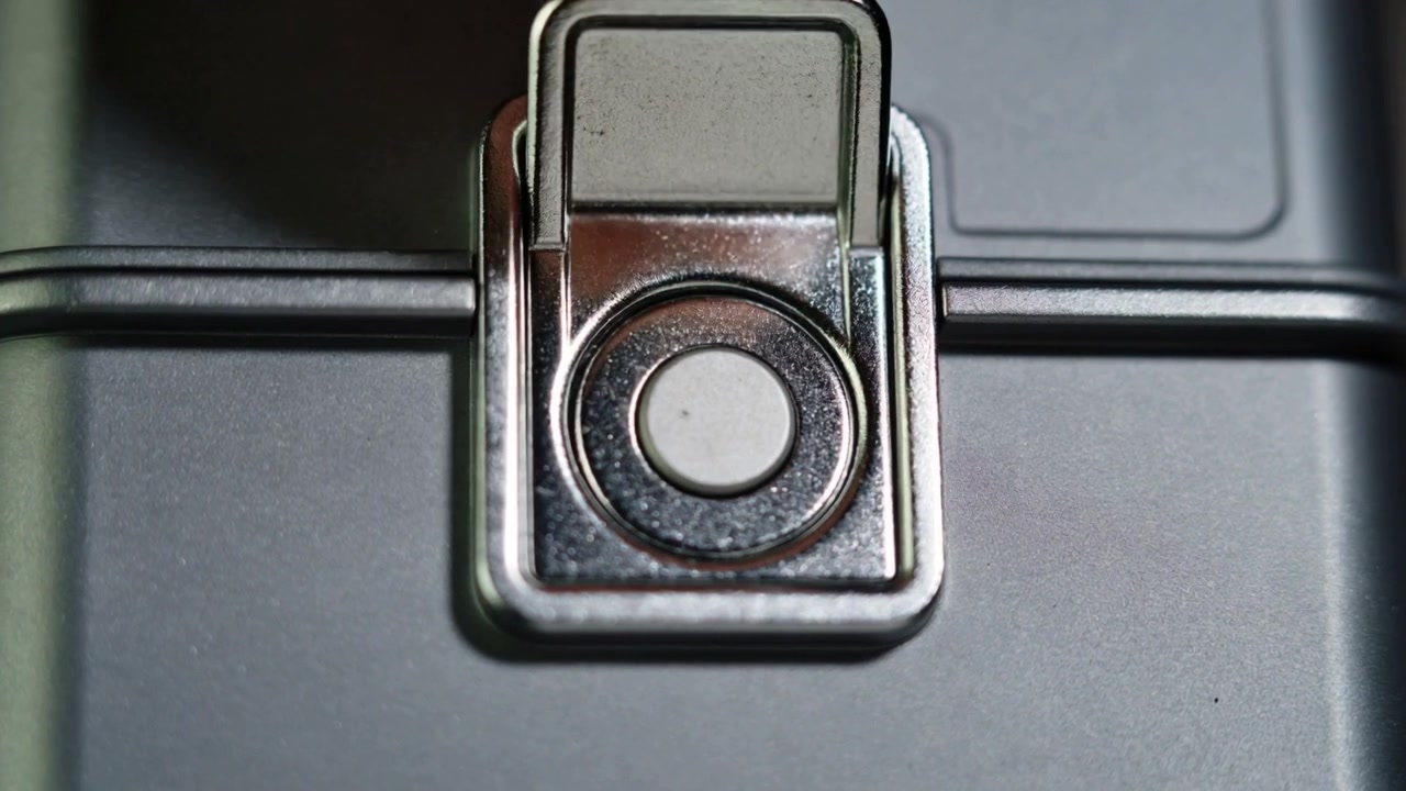 Pressing fingertip on circular release, latch closing on gray case with hinged hasp sealing