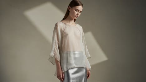 Elegance in Soft Fabric: A Model Showcases a Sheer Blouse and Metallic Skirt, Capturing Modern Fashion Aesthetics in a Minimalist Setting