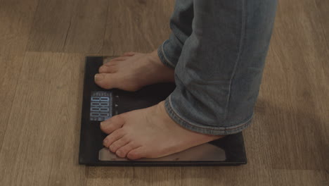 High-angle-view-of-bare-feet-stepping-onto-weight-scale