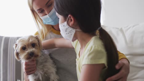 madre e hija con máscaras faciales abrazando a su perro doméstico en casa