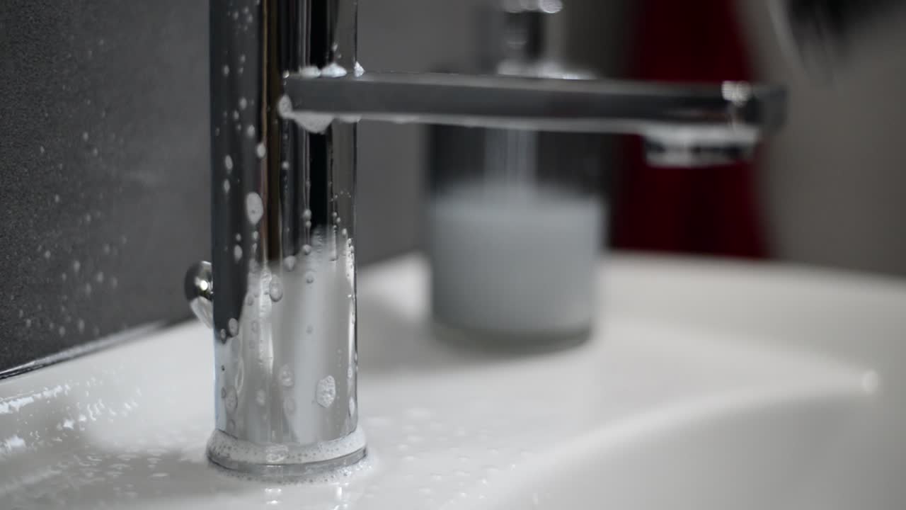 Rubinetto cromato spruzzato con detergente per il bagno e pulito con uno straccio grigio.