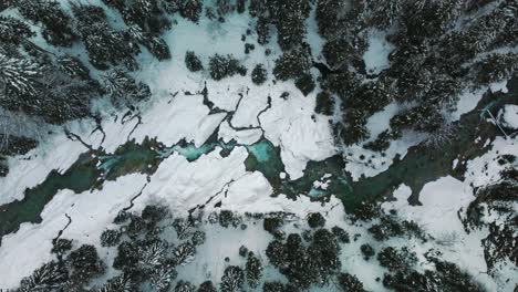 cinemagraph aerial seamless video loop of a scenic and idyllic mountain river waterfall canyon in winter with ice, snow and fresh blue frozen water in the bavarian austrian alps, flowing down a natural forest along trees seen from aerial view perspective.