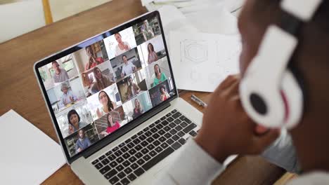 estudiante universitario afroamericano que sostiene notas y tiene una videoconferencia en una computadora portátil en casa