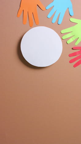 vertical video of hands around circle made of colourful paper on brown background with copy space
