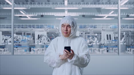 asian male scientist using smartphone and look around while standing in modern lab factory with automated robots