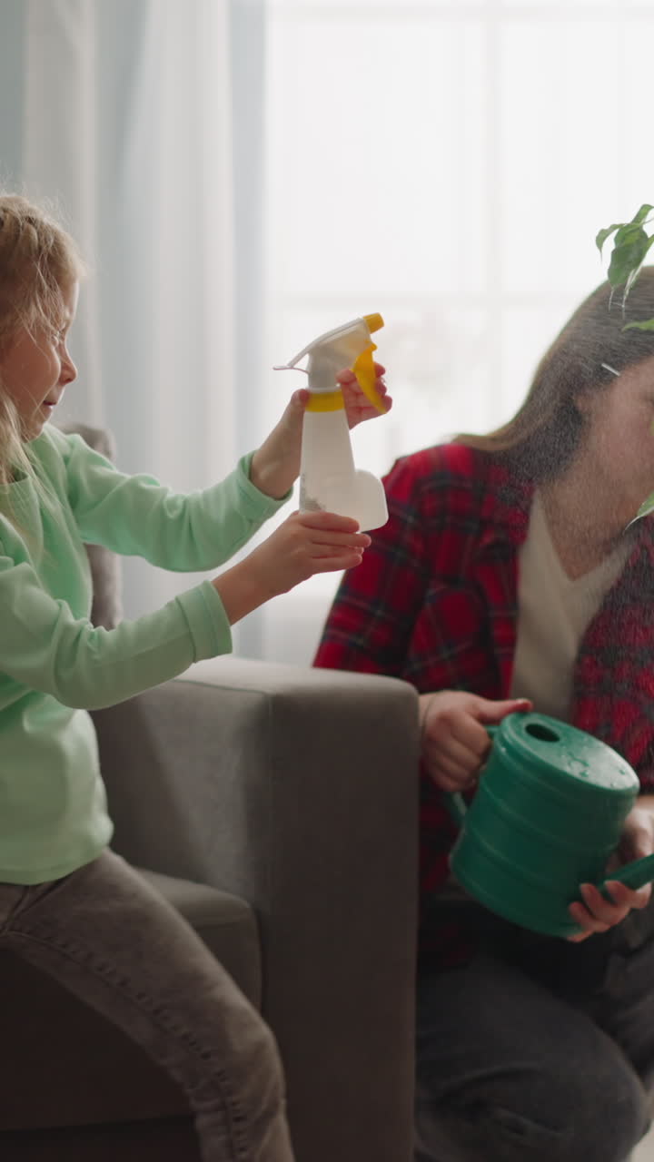 la niña bailarina pulveriza ficus en la sala de estar en cámara lenta. la hermana mayor riega la planta en olla en el hogar. cuidado profesional de la planta de interior tropical