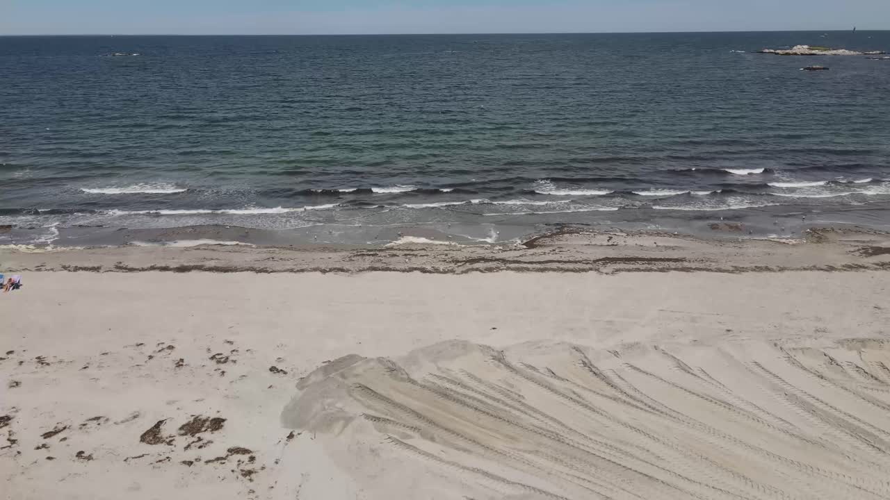 매사추세츠주 코하셋의 모래사장에 있는 중장비 바퀴를 배경으로 대서양 파도가 있는 트랙