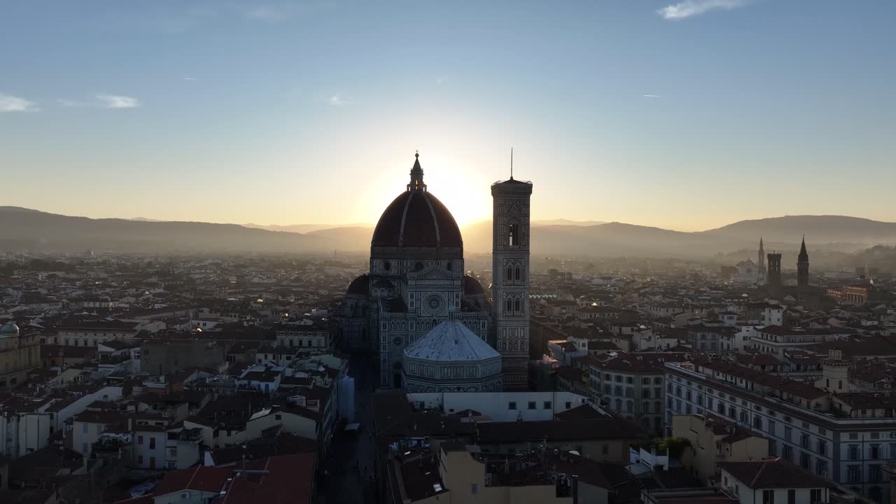 High-angle aerial panorama of the Florence Cathedral, Giotto's Campanile, and the historic city center, silhouetted against a bright sunrise and sun flare