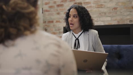 diverse female colleagues in discussion using laptop in office lounge, slow motion