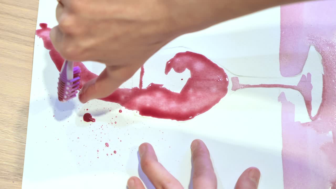 A woman in a studio painting on paper with red wine and toothbrush, close view