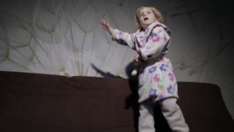 little cute girl with blond hair jumps on sofa. bathrobe clothes. happy