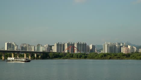 el crucero en ferry se mueve en el río hangang desde el puente seogang a lo largo de la isla bamseom con edificios de apartamentos urbanos de gran altura en seúl y montañas bukhansan en el fondo, turismo en corea del sur durante el día