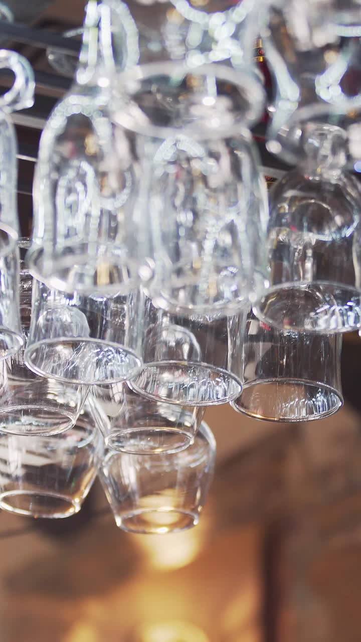 Empty crystal glasses hang at the glassware holder at bar counter. Beautiful new glasses from glass hanging in even rows. Vertical video.