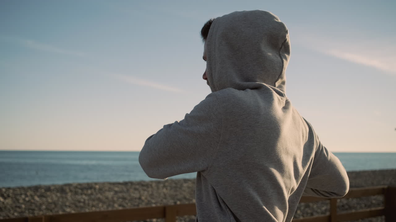 해가 지는 해변에서 운동하는 후디를 입은 남자