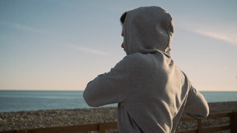 hombre con una sudadera con capucha haciendo ejercicio en una playa al atardecer
