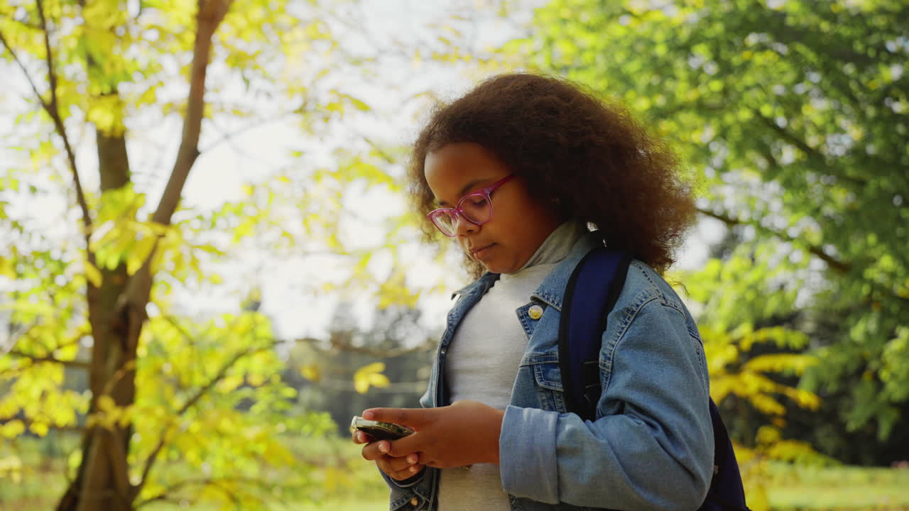 Young African American Girl Using Smartphone in Autumn Park