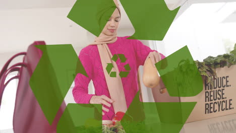 biracial woman in hijab taking vegetables out of box in kitchen over recycling sign