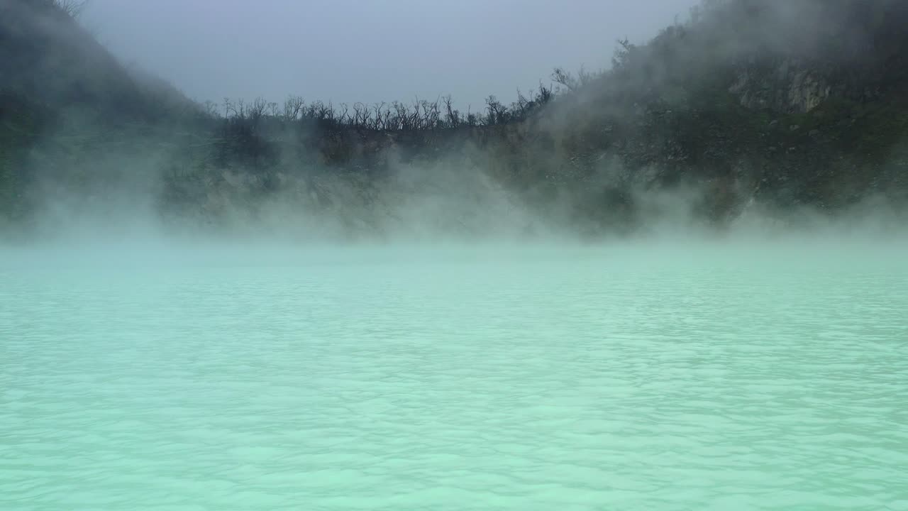 spooky landscape with steam rising from green sulfur lake in Kawah Putih volcano crater in Bandung Indonesia