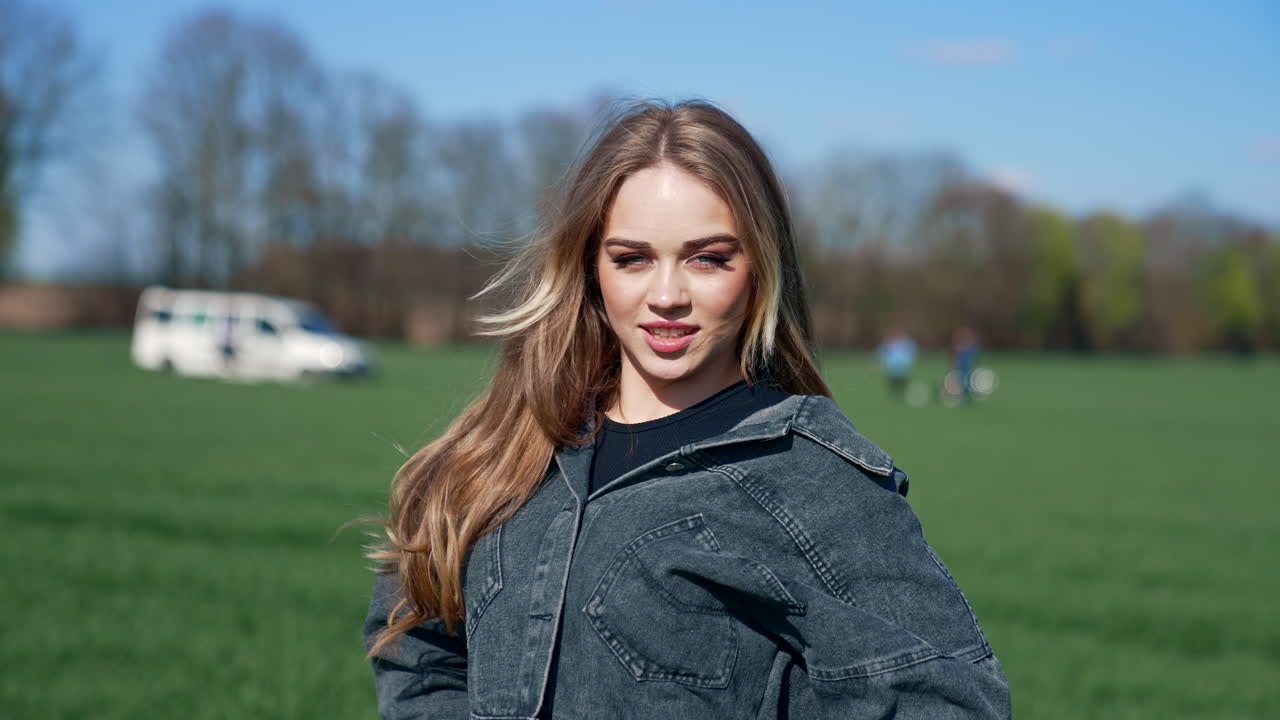 Happy girl on a meadow. Attractive young model with lovely face in denim suit posing on camera and smiles. Portrait of a young woman in nature in a sunny day