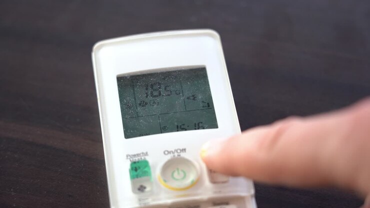Finger trykker på varmepumpens fjernbetjening for at øge rumtemperaturen – Nærbillede af fjernbetjening med sløret finger og temperatur i fokus