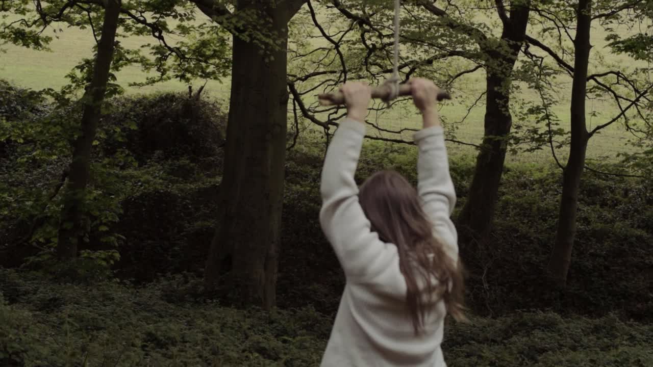 Woman swinging on homemade rope swing in woodland wide shot