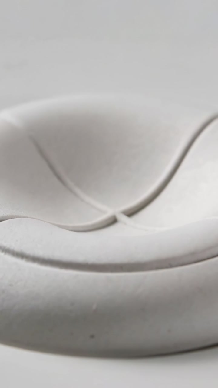 Vertical video: Tapping, pressing right fingertip creating pleats on white soft disc on gray table