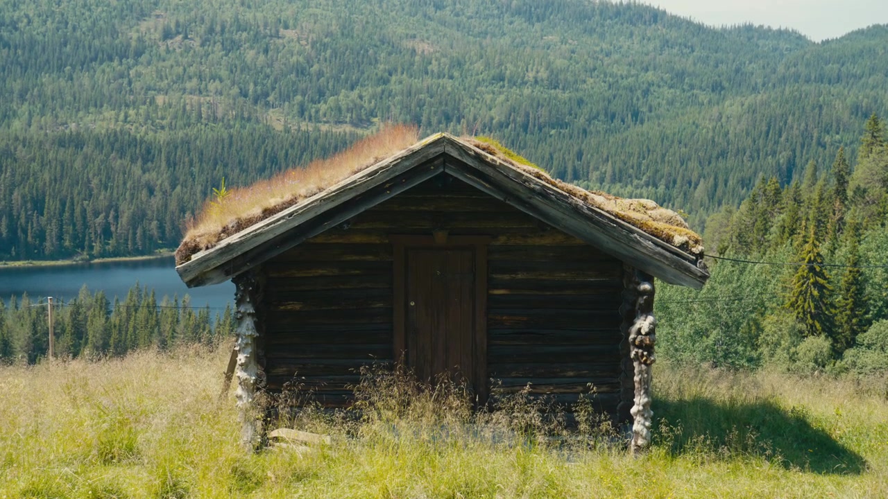 Tradisjonelt norsk tre-stabbur med torvtak omgitt av fjellandskap, skog og innsjø, som viser nordisk bygdekultur