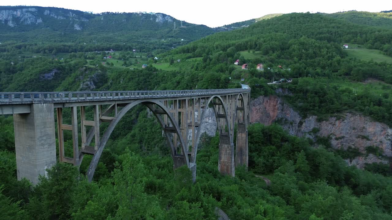 The Tara Bridge, a concrete arch bridge surrounded by lush forests within Durmitor National Park, Aerial revealing shot