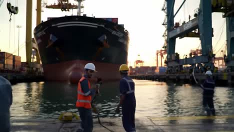 dockworkers coordinating operations as a cargo ship arrives at the port, highlighting maritime industry and ship loading activities during sunset