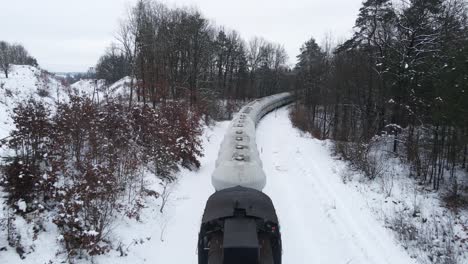 Drone-Siguiendo-Un-Largo-Tren-De-Carga-A-Través-De-Un-Bosque-Nevado-En-El-Distrito-De-Kashubian,-Polonia