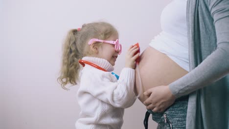 una niña juguetona examina a su madre embarazada con juguetes en casa