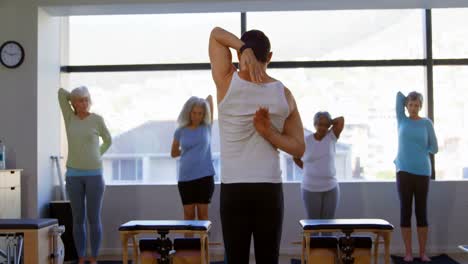 Trainer-assisting-senior-women-in-performing-yoga-4k