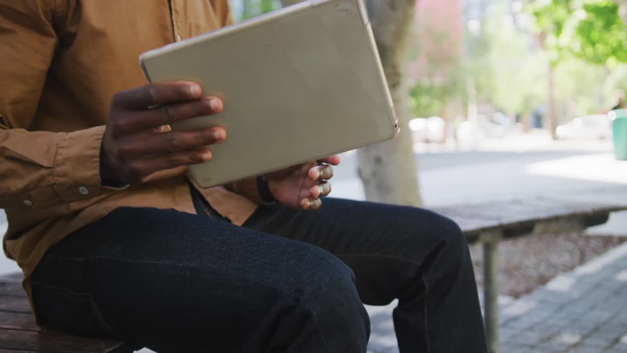 Midsection of african american businessman putting tablet in bag sitting on bench
