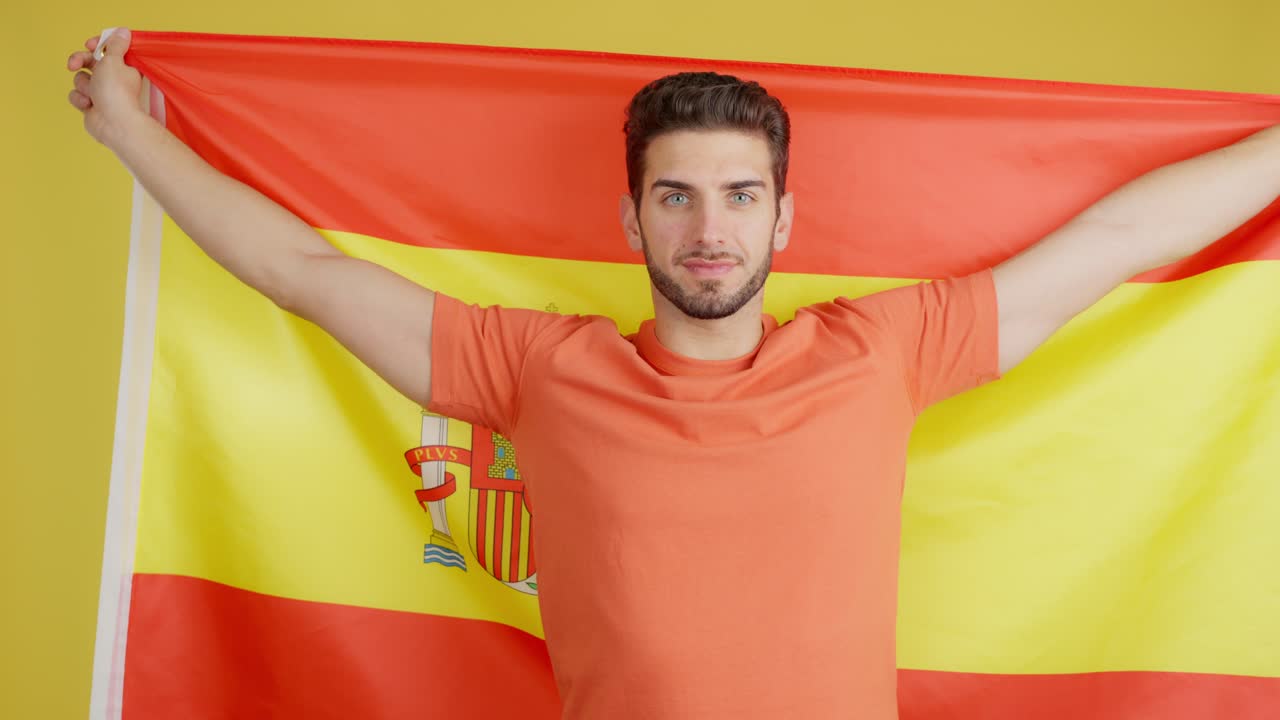 Smiling Young Man Wrapped in Spanish Flag on Yellow Background