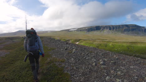 male hiker walking in saltoluokta, northern sweden. snow on mountain and green grass in the background.