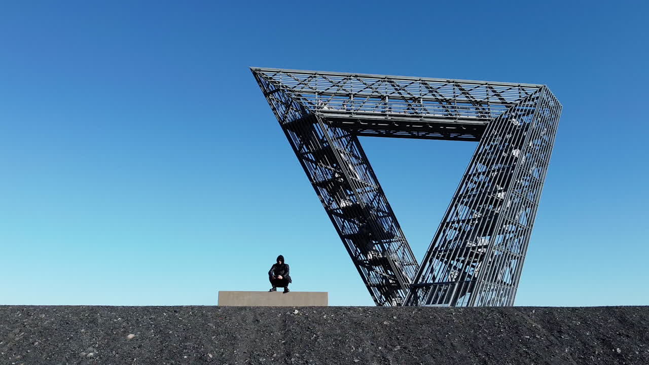Person Sitting in Front of a Large Metal Triangular Structure