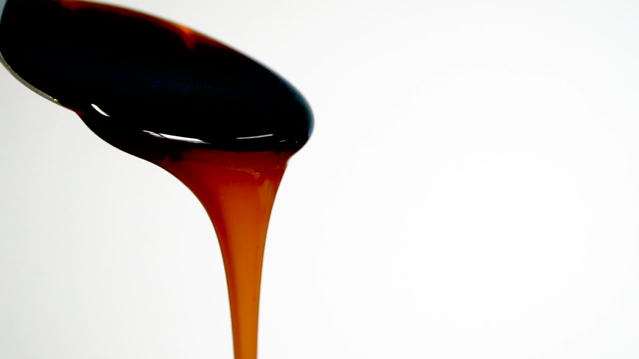 Molasses pours from spoon, slow motion, close up