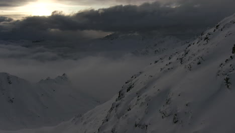 Cinematic-drone-shot-of-snowy-mountains-above-cloudscape-during-sunset-time-mid-winter-Austrian-Alps-Kauntertal,-Austria