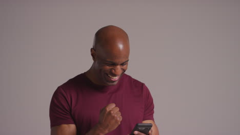 studio shot of excited mature man with mobile phone celebrating winning money against grey background 3