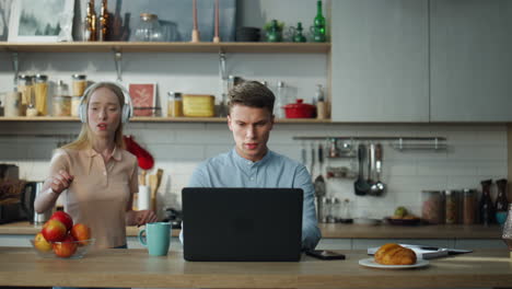 programador serio trabajando remotamente en la cocina. mujer bailando cerca de marido ocupado.