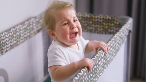 side view of crying baby in white bodysuit inside the baby playground while his mother giving him a fruit