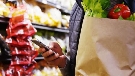 hombre usando teléfono móvil mientras sostiene una bolsa de comestibles