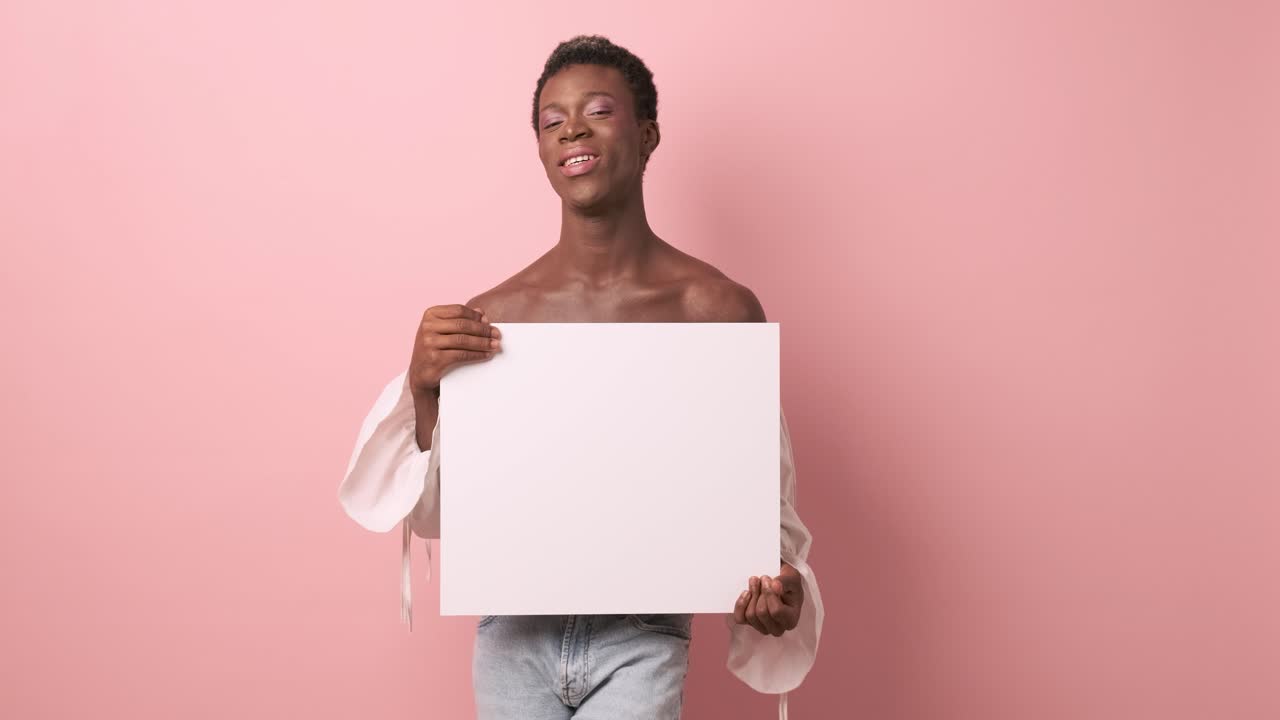 African transgender person smiling while holding a blank white poster.