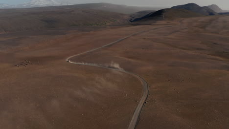 Establishing-shot-aerial-view-car-driving-gravel-trail-path-in-Icelandic-dusty-desert.-Drone-view-4x4-vehicle-speeding-desolate-vibrant-red-sand-landscape-stirring-up-dust-cloud.-Insurance-commercial