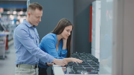 young couple chooses cooktop in store of household appliances